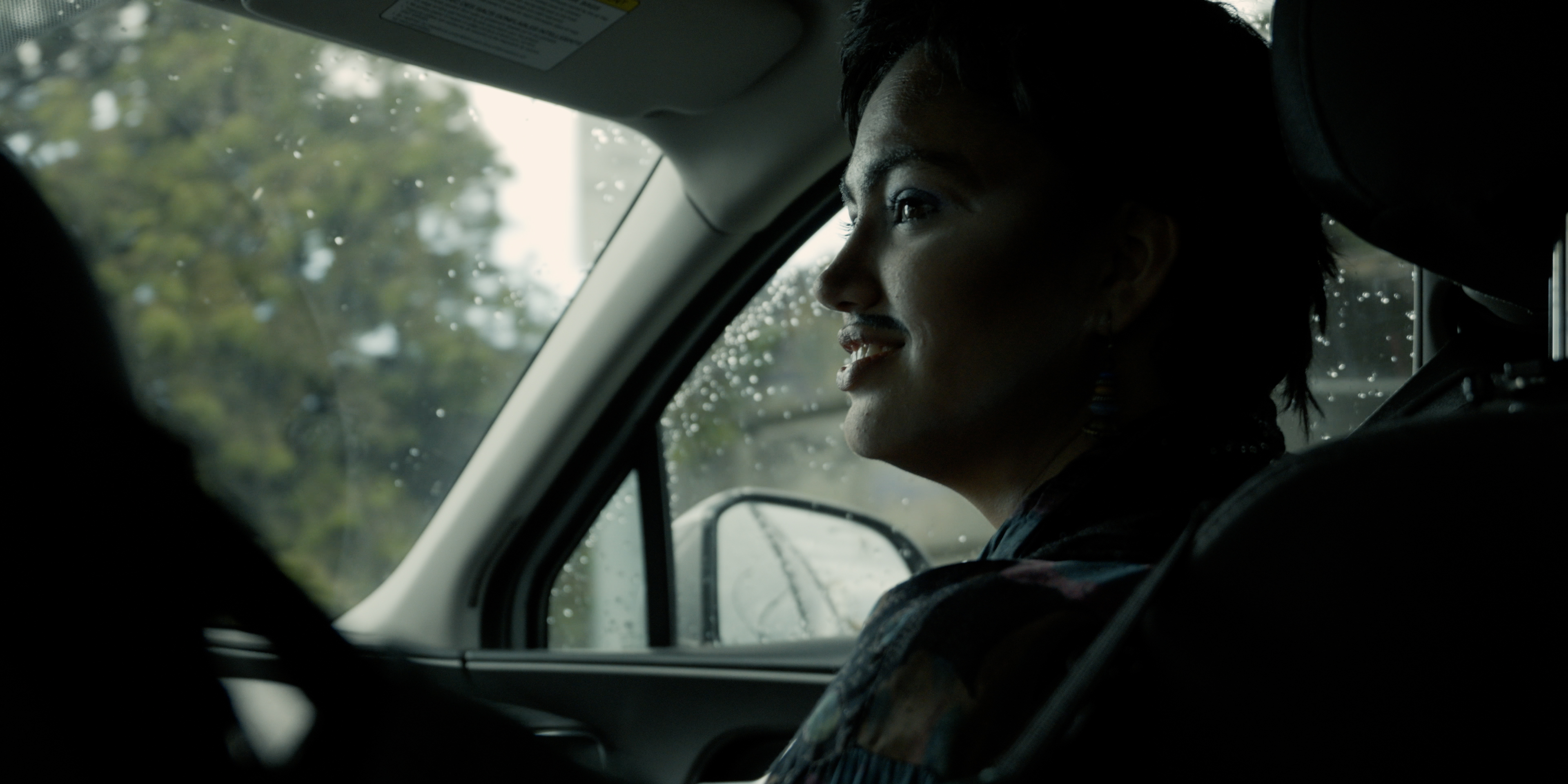 Performer with a drawn moustache sitting inside a car on a rainy day in Victoria Ka Raja