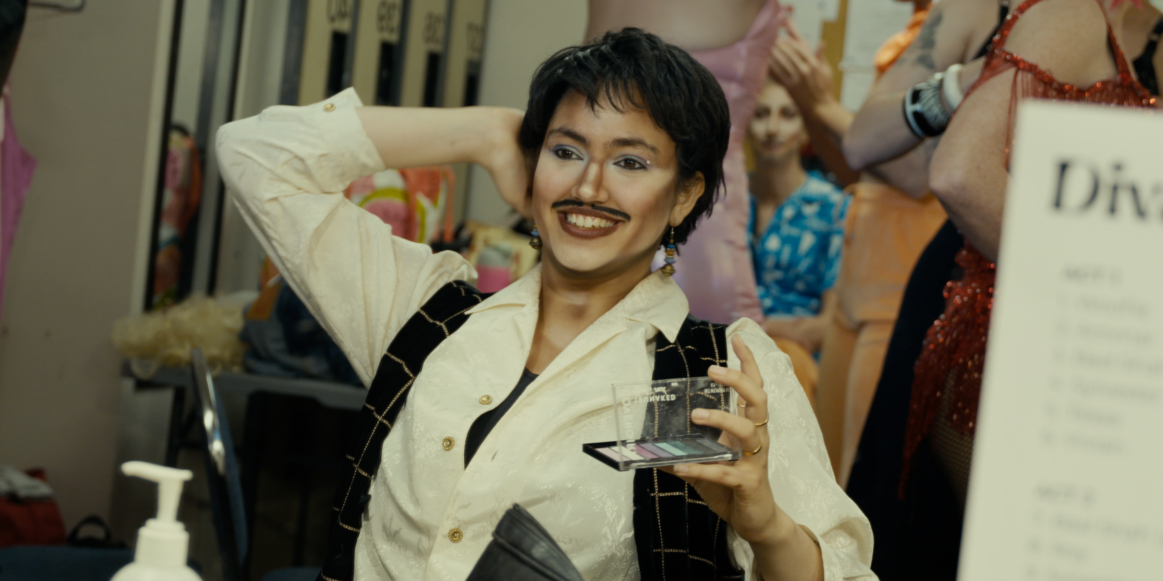 Drag king smiling while holding a makeup palette backstage in Victoria Ka Raja