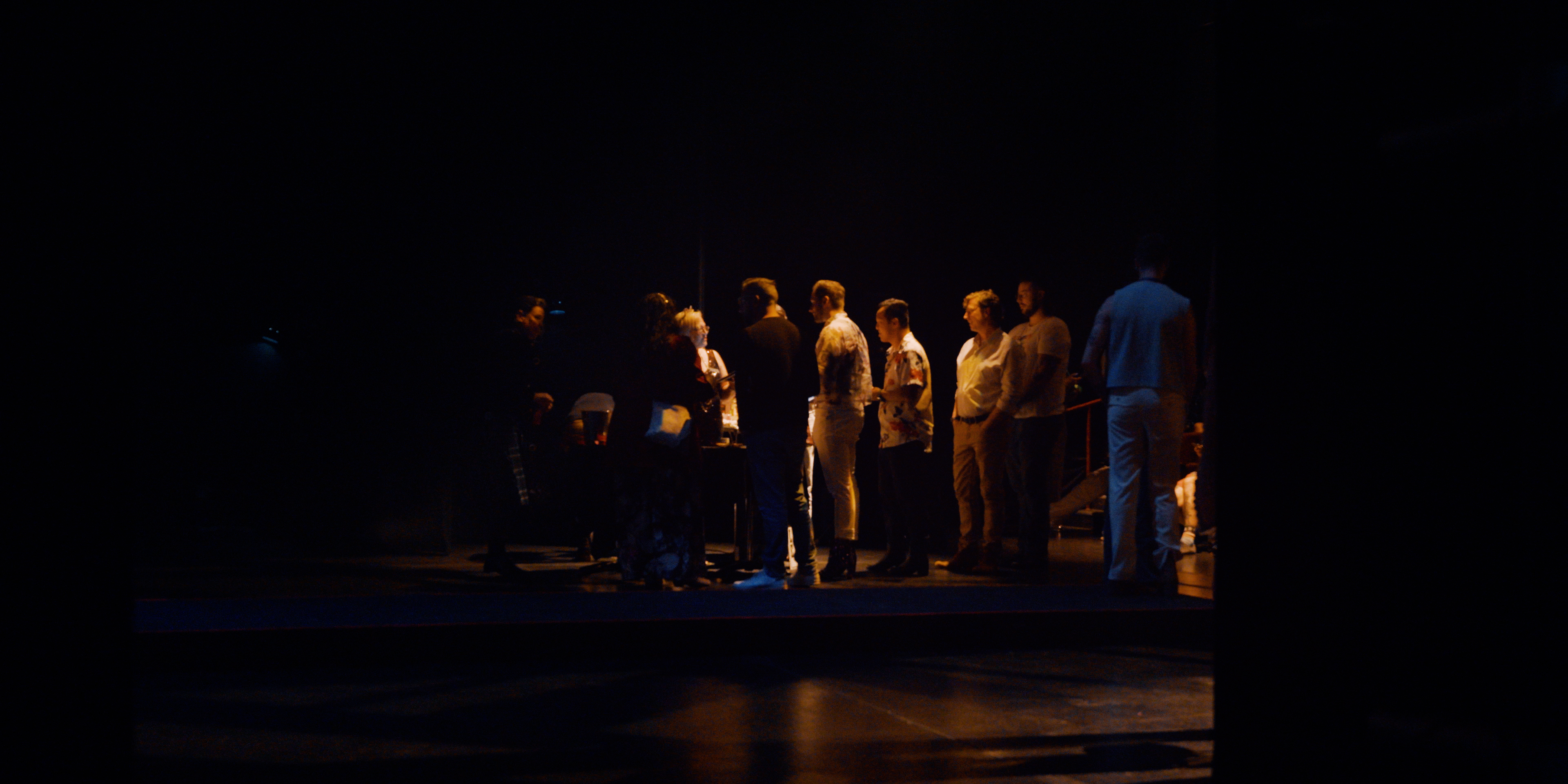 Performers gathered together on a dark theatre stage in Victoria Ka Raja